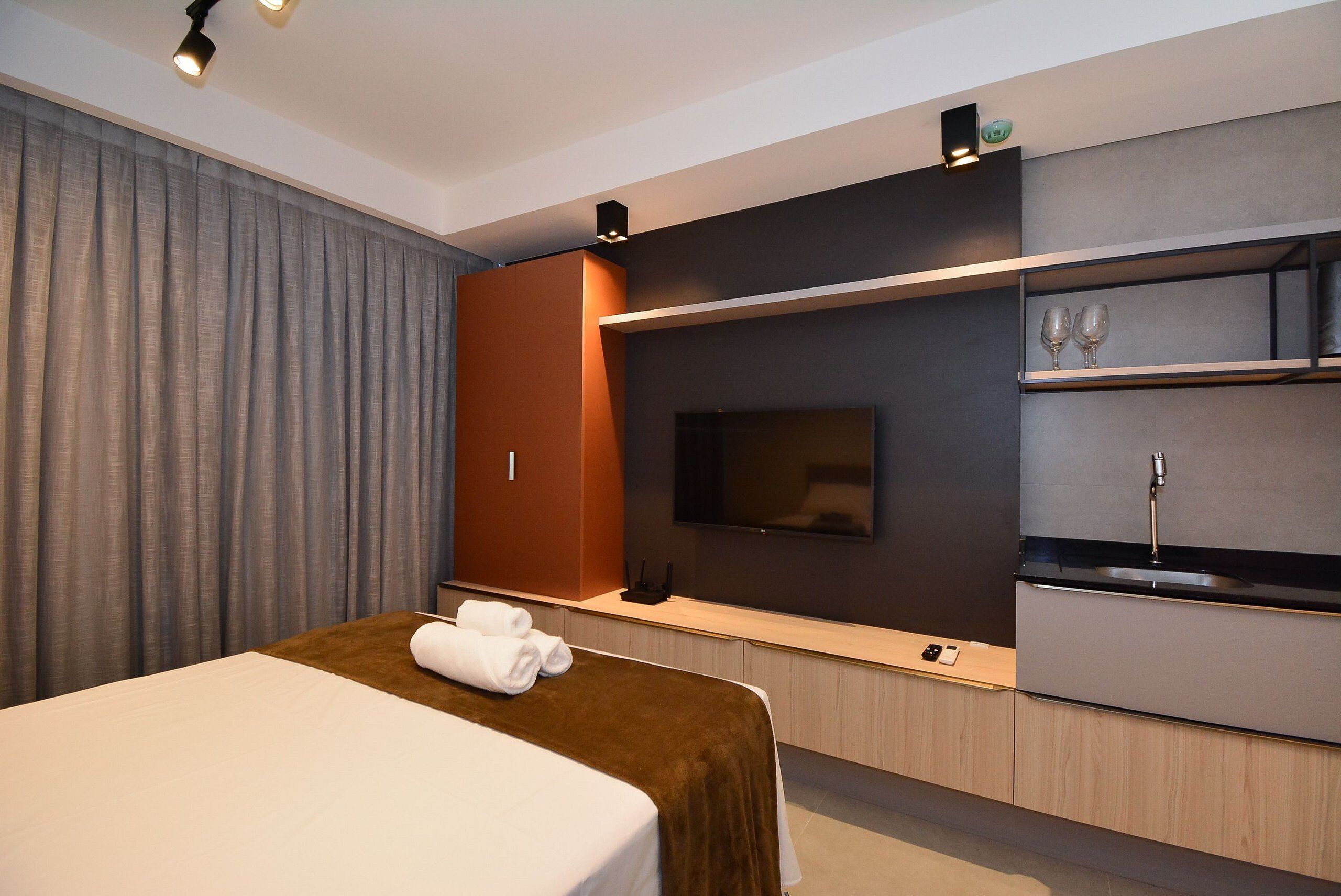 A modern hotel room with a bed, a television, a minibar, and a built-in oven.
