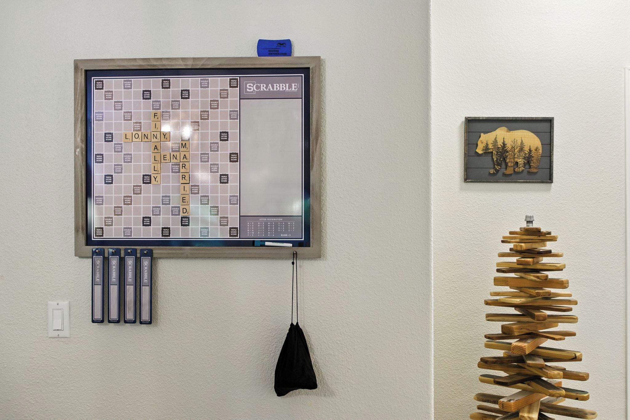 Seinälle asennettu Scrabble-lautapeli, karhuaiheinen taideteos ja puuveistos.