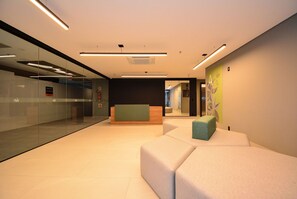 Un lobby moderno con paredes de vidrio, una recepción y una zona de estar con cojines.