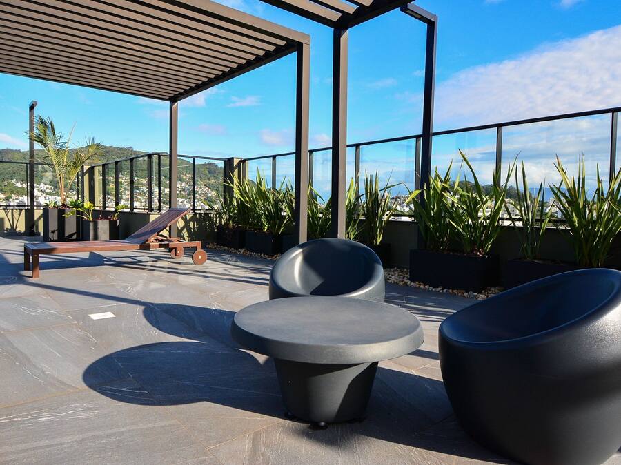 An outdoor seating area with modern chairs and a bench, surrounded by potted plants and a view of a cityscape.