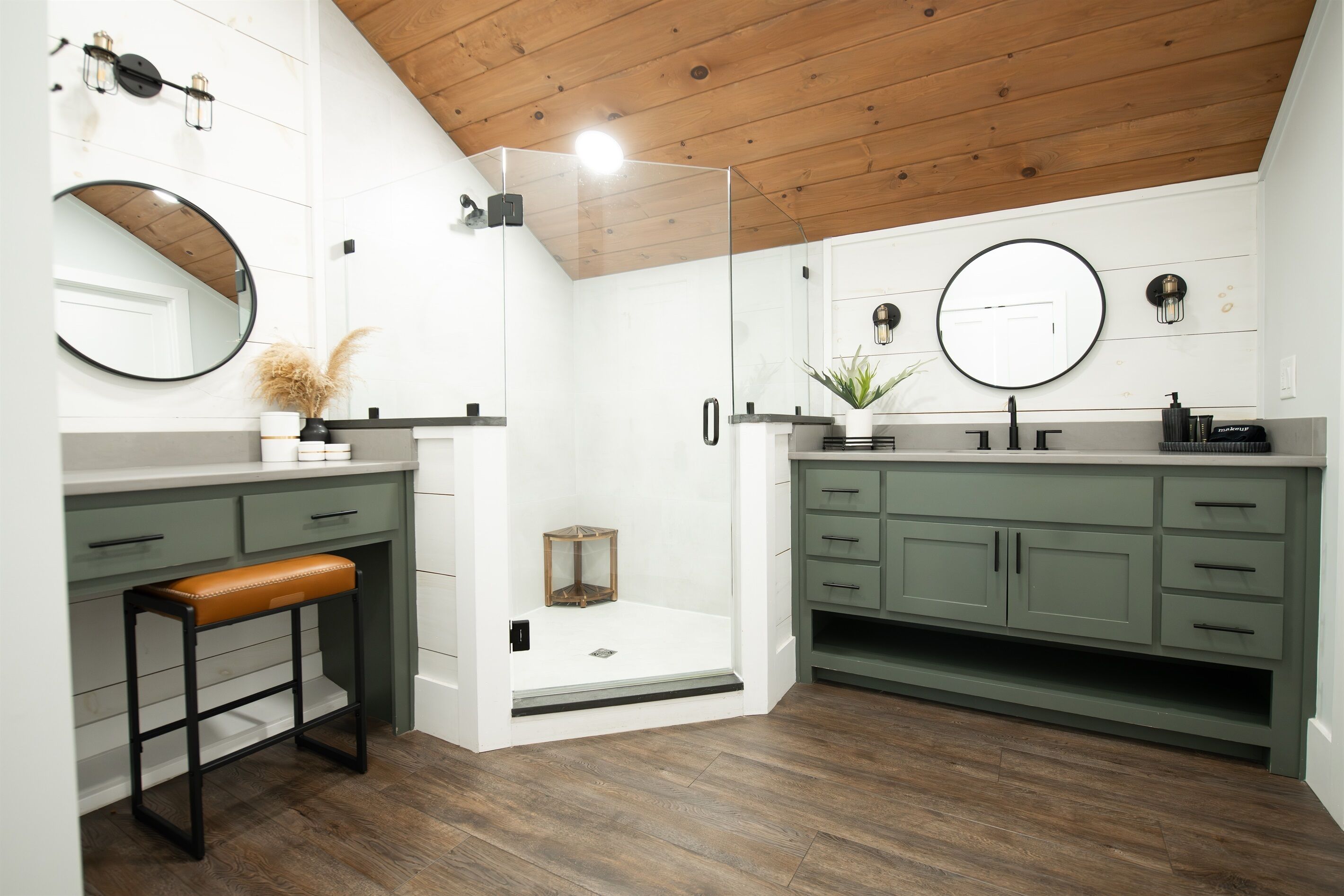 A modern bathroom with a wooden ceiling, two sinks, a bench, and a glass shower enclosure.