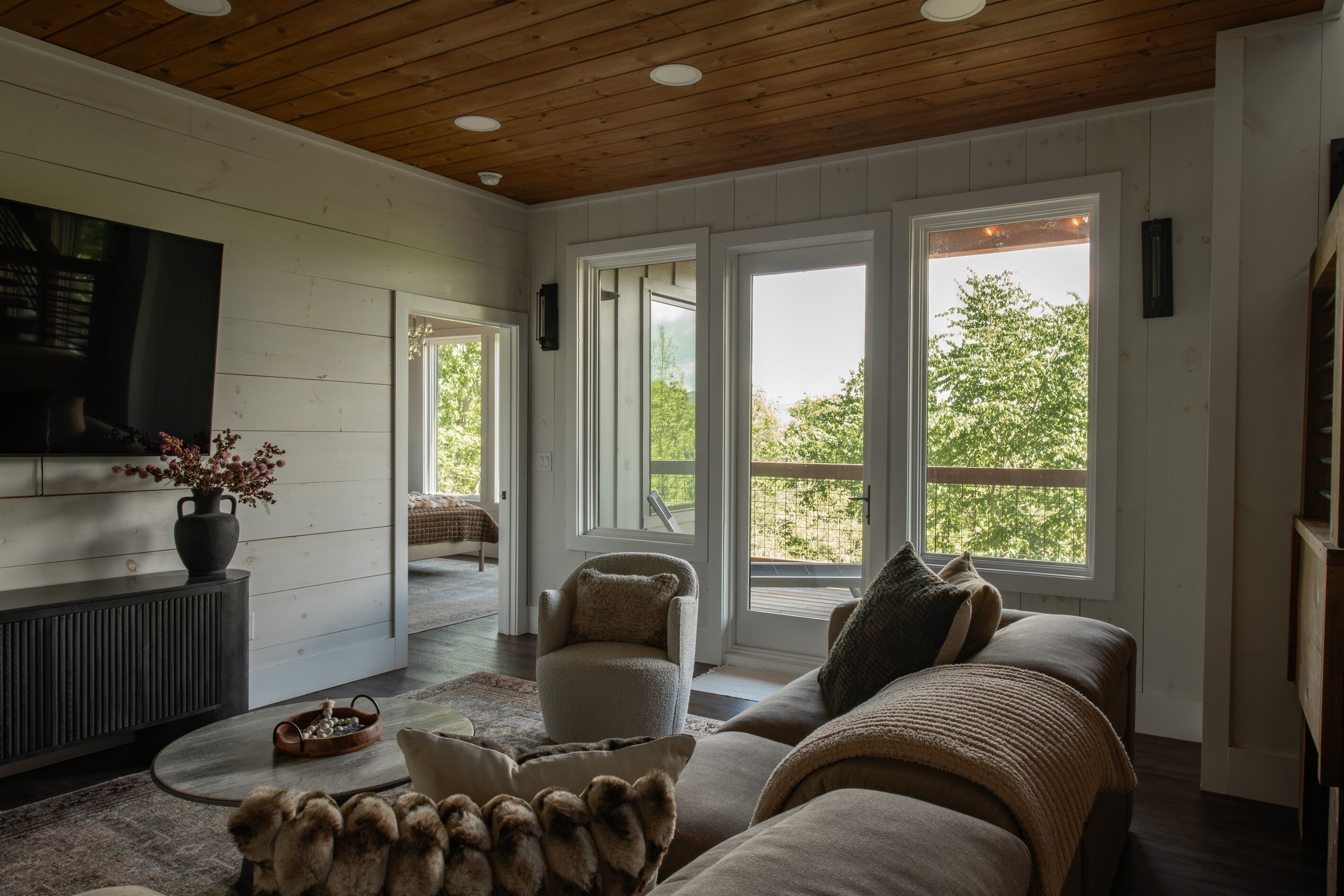A cozy living room with a fireplace, comfortable seating, and large windows offering a view of the outdoors.