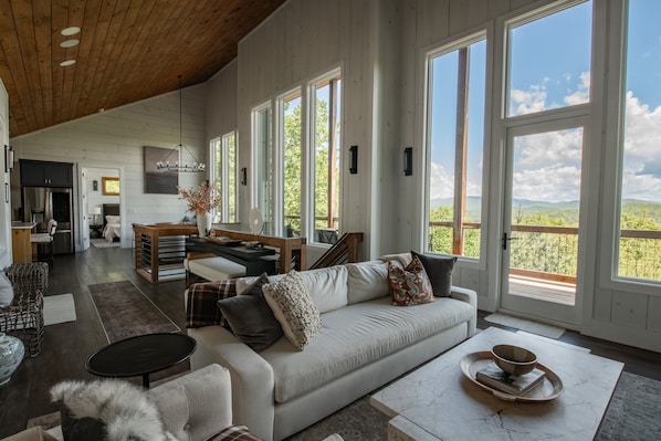 Ein geräumiges Wohnzimmer mit einem großen weißen Sofa, einem Essbereich und Blick ins Freie.