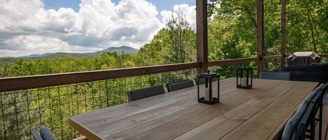 A wooden deck with a table and chairs, overlooking a mountainous landscape.