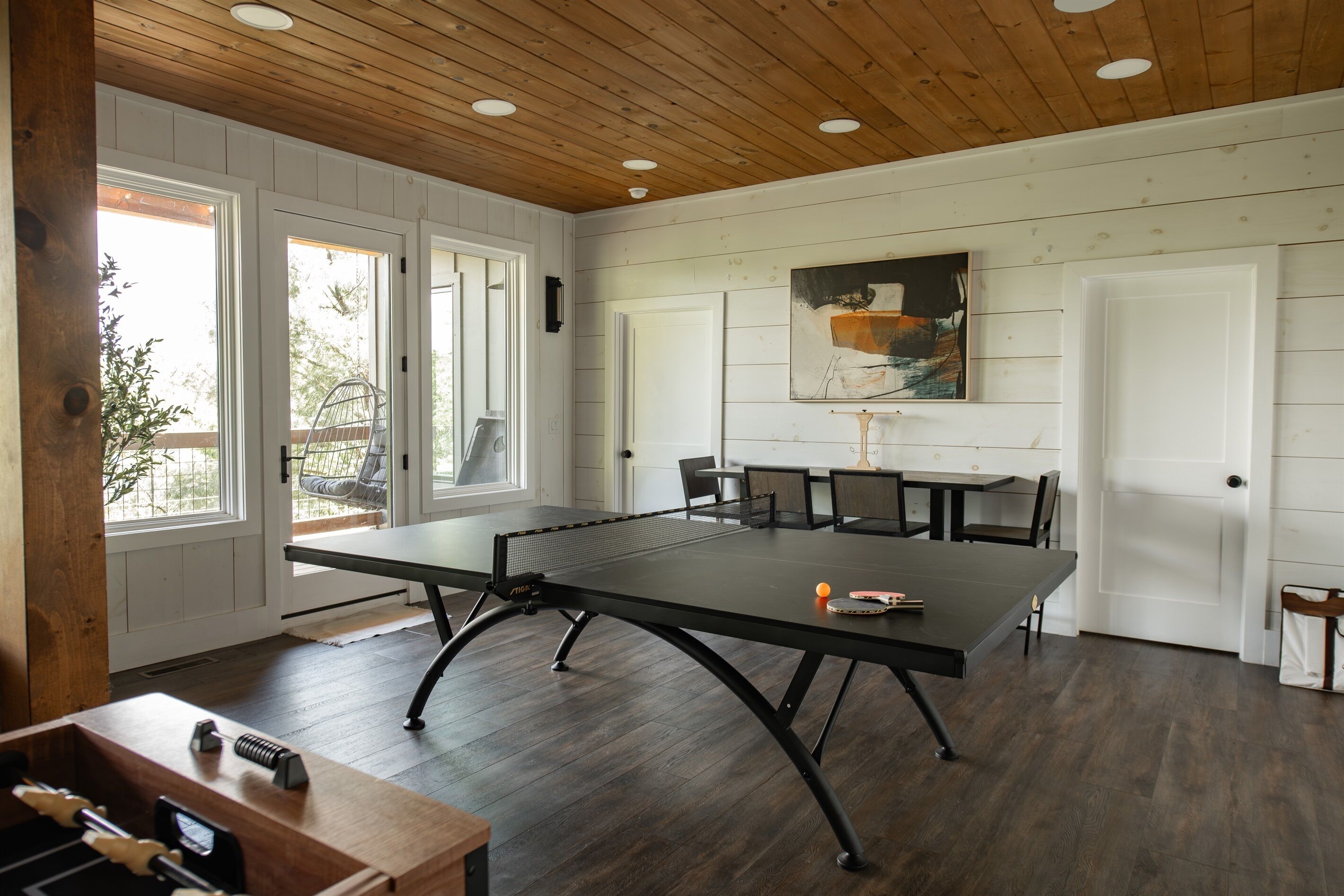 Une pièce avec une table de ping-pong, des chaises, un baby-foot et un tableau accroché au mur.