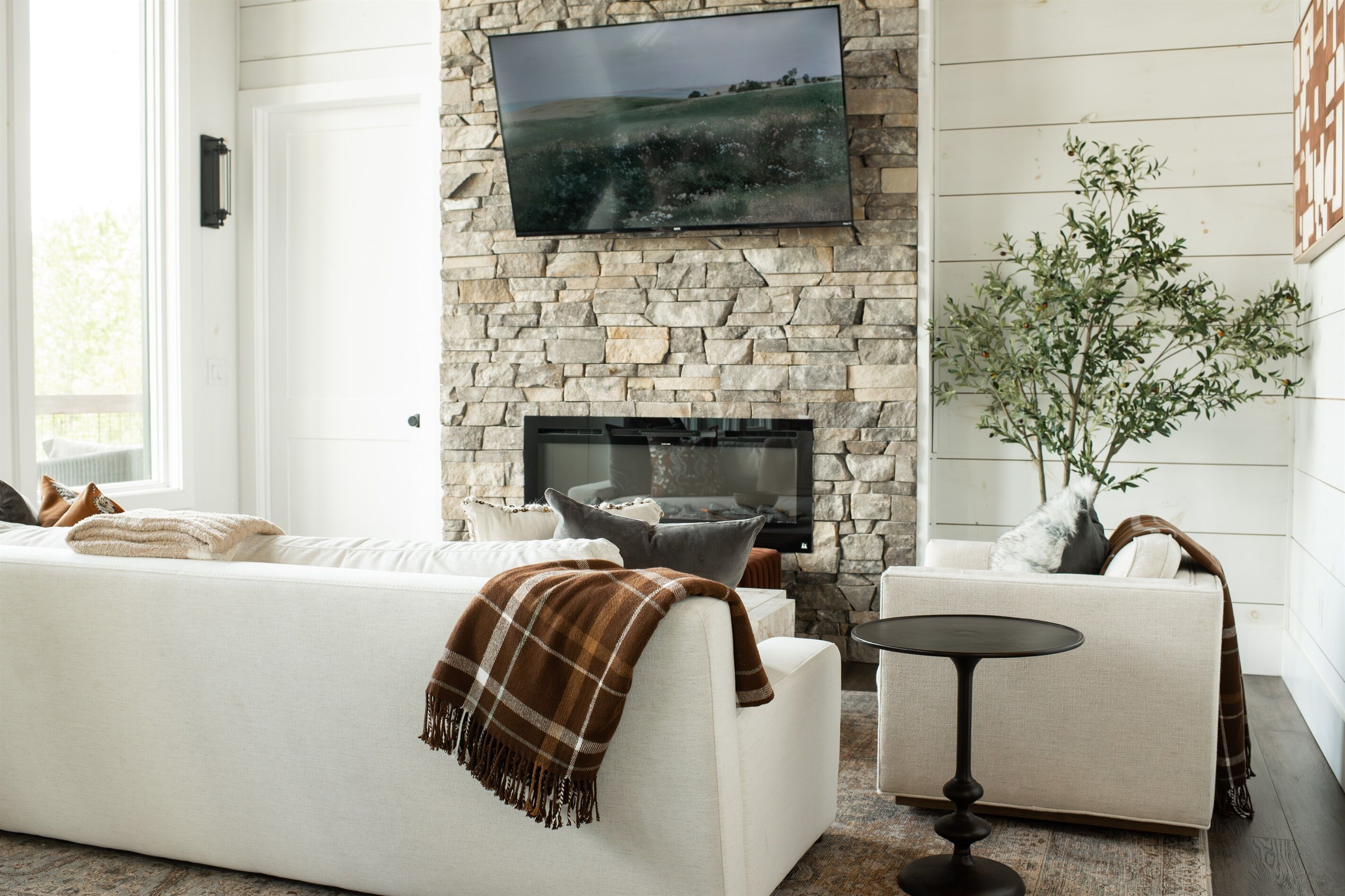 Una sala de estar con chimenea de piedra, un televisor de pantalla plana, un sofá, una butaca y una mesita.