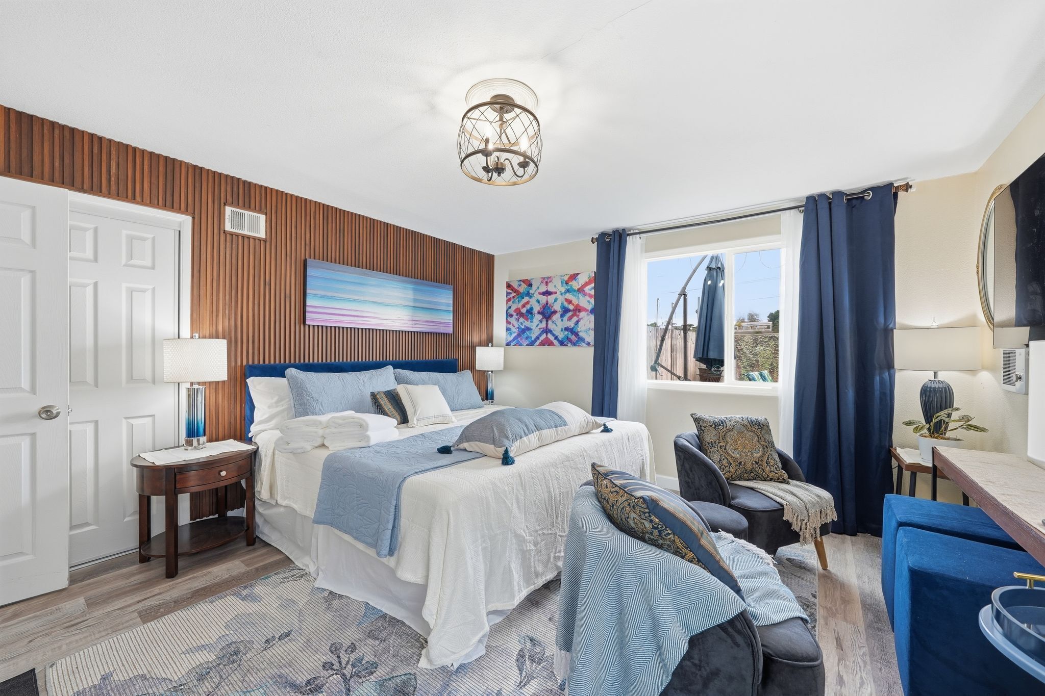 Un dormitorio con cama, mesitas de noche, una silla, un escritorio y una ventana con cortinas.
