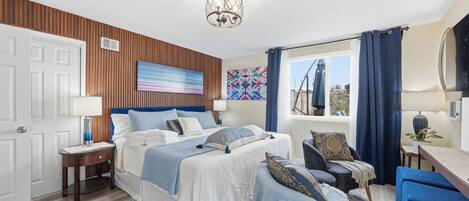 Un dormitorio con cama, mesitas de noche, una silla, un escritorio y una ventana con cortinas.