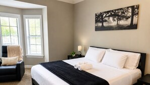 A hotel room with a large bed, a chair, a nightstand, and a painting on the wall.