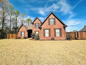 A two-story brick house with a front garage, a fenced yard, and a clear blue sky.