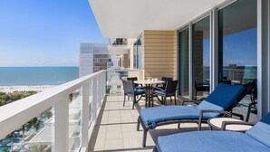 A balcony with a view of the beach, a table with chairs, and a lounge area with blue cushions. - Marriott’s Crystal Shores: 2 Bedroom Poolside Paradise Awaits on Marco Island (Marco Island)