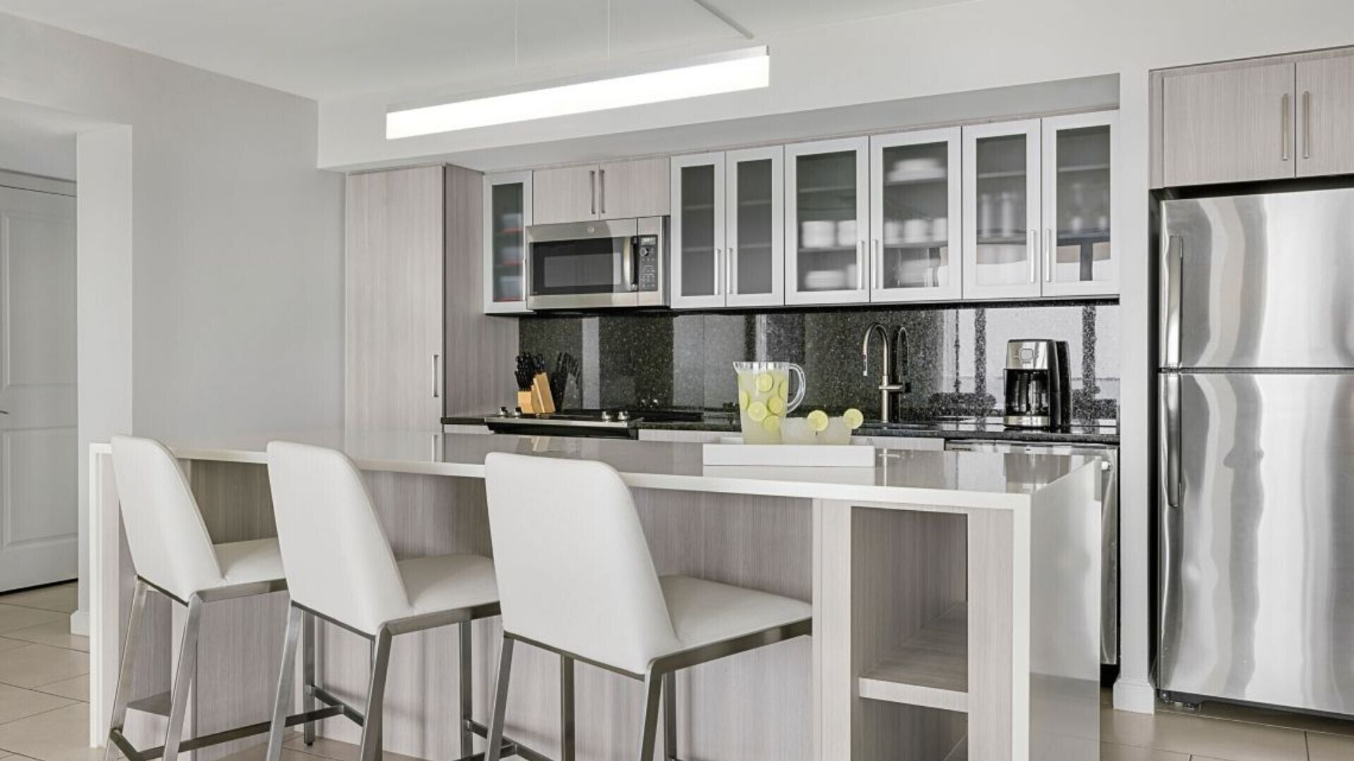 A modern kitchen with a central island, bar stools, stainless steel appliances, and a coffee maker.