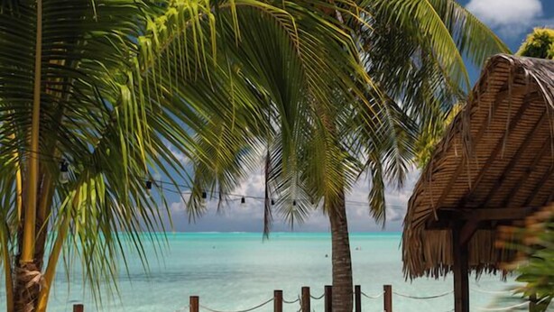A beachside lounge with lounge chairs, palm trees, and a thatched-roof structure. - Matira Sunset House (Bora Bora)