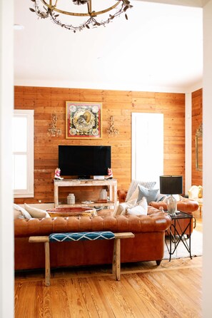 A cozy living room with a leather sofa, a television on a wooden stand, and a decorative painting on the wall.