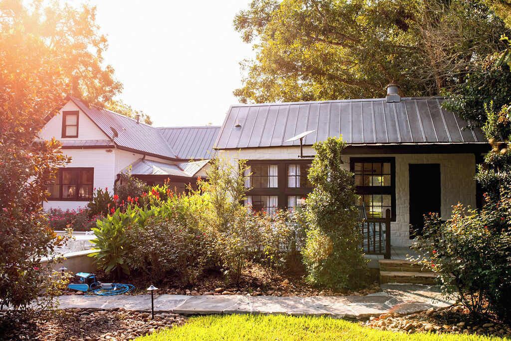 A two-story house with a garden in front, a visible water feature, and a hose on the ground.