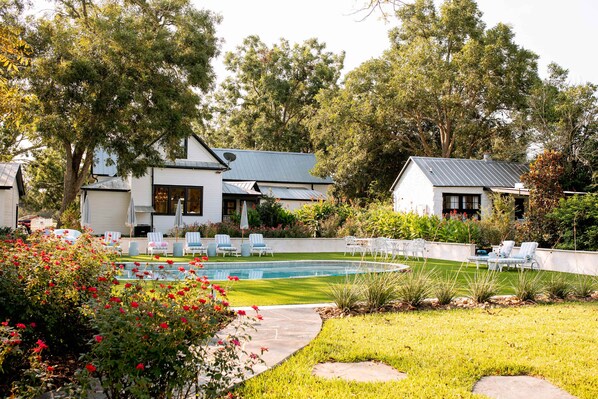 A residential property with a swimming pool, outdoor seating, and lush greenery. - RT Cottage for 2 in Town | Pool+Pickleball+Firepit (Round Top)