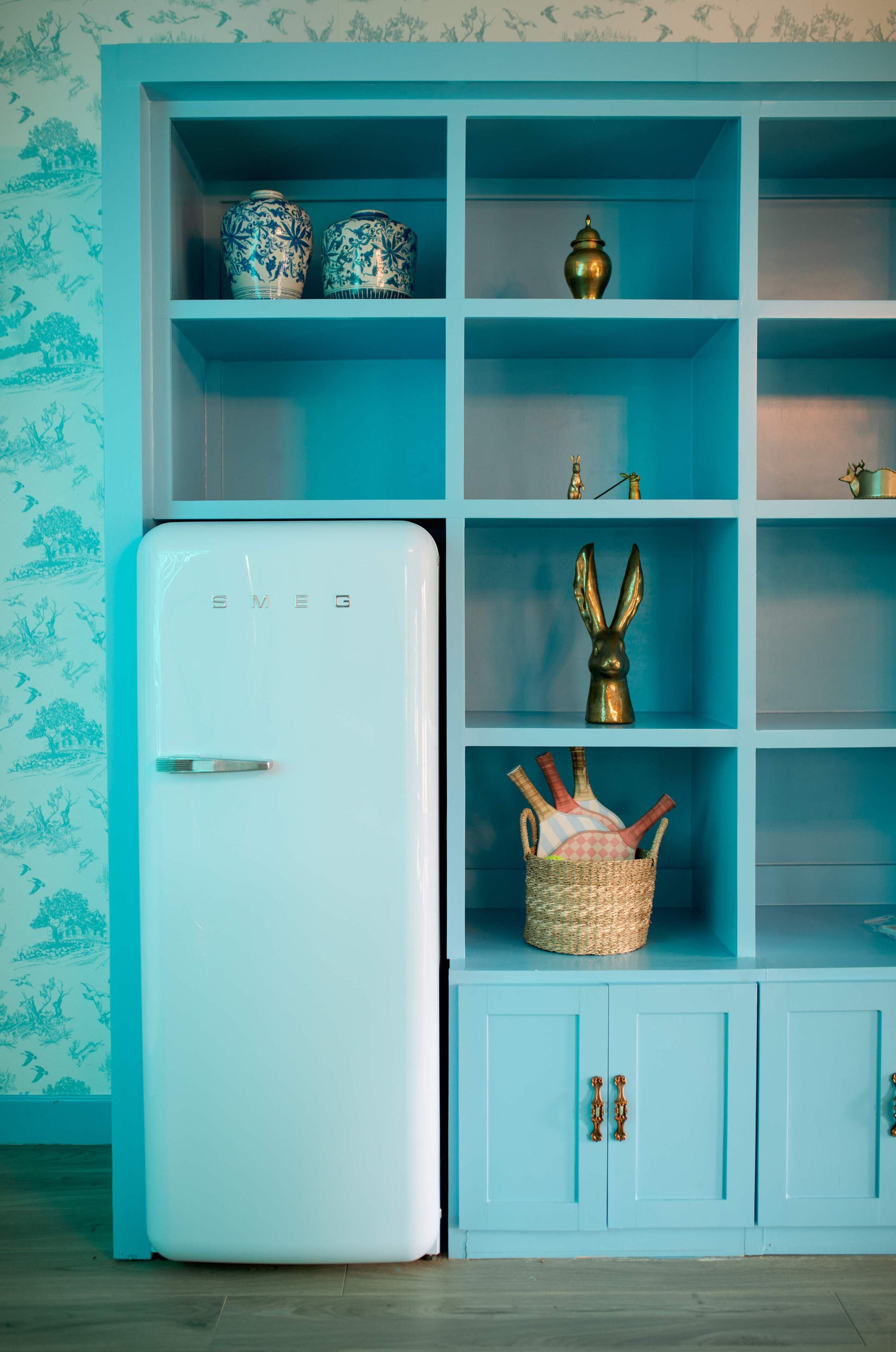 A room with a white refrigerator, a blue cabinet with shelves, and a patterned wallpaper.