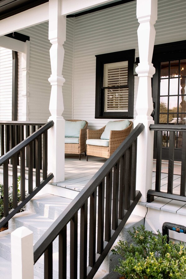 A covered porch with a staircase, a seating area with wicker furniture, and a window with blinds.