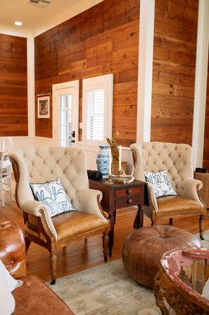 A room with two upholstered chairs, a small table with decorative items, and a wooden floor. - Pool + Pickleball + Firepit | IN TOWN | Sleeps 8 (Round Top)
