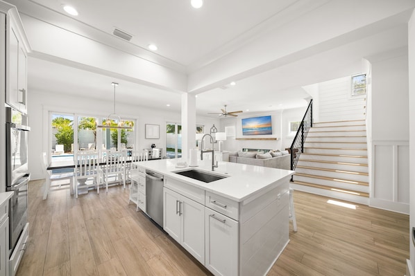 A spacious kitchen with white cabinetry, a central island, and a dining area with white chairs. - Hilltop Haven with LSV, Spa, and Accessible Beach (Santa Rosa Beach)