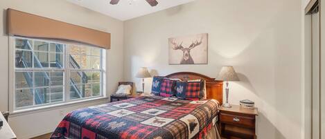 A bedroom with a large bed, a ceiling fan, a window with a view of a staircase, and a deer painting on the wall.