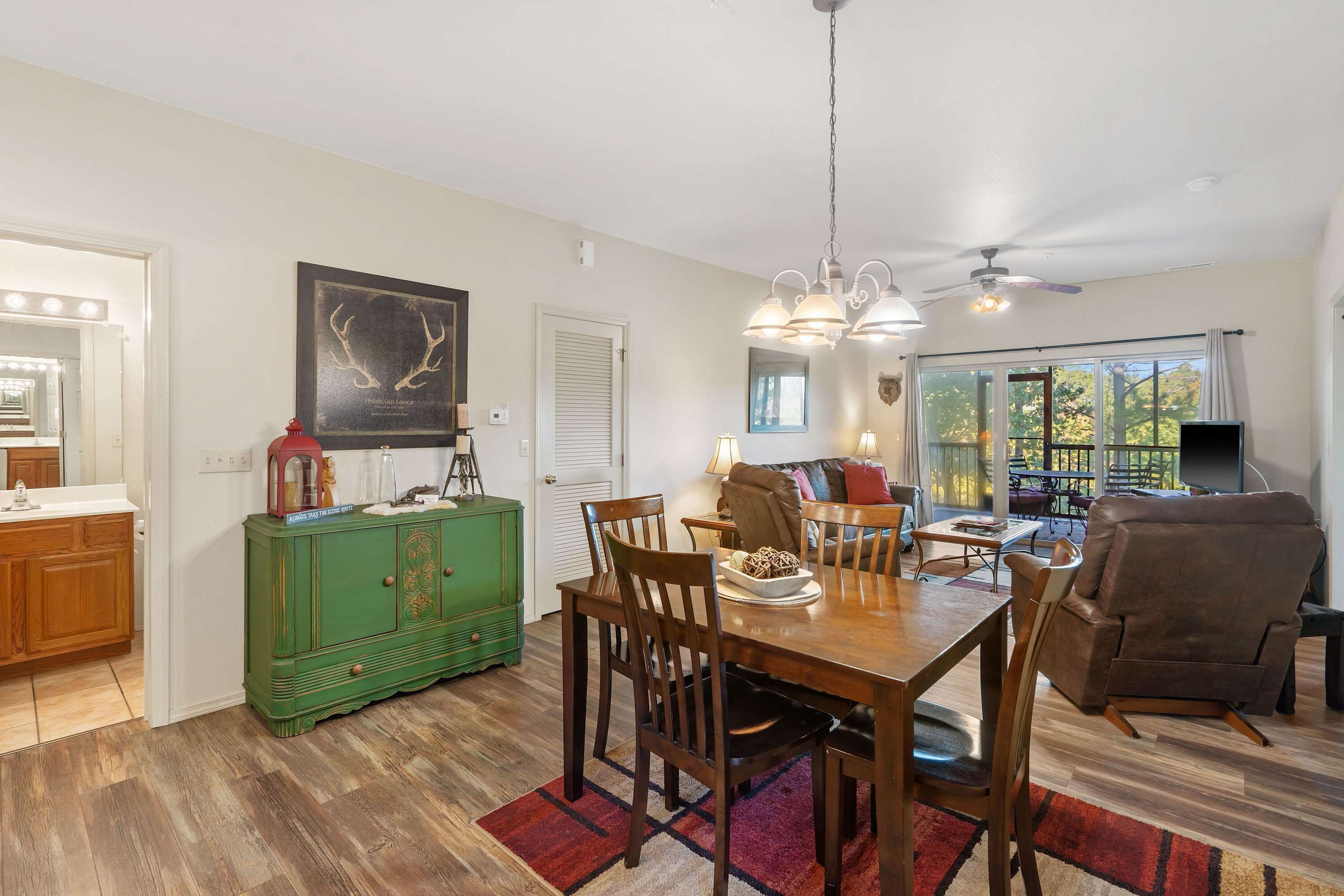 A spacious living area with a dining table, chairs, a green cabinet, and a large window offering a view of the outdoors.