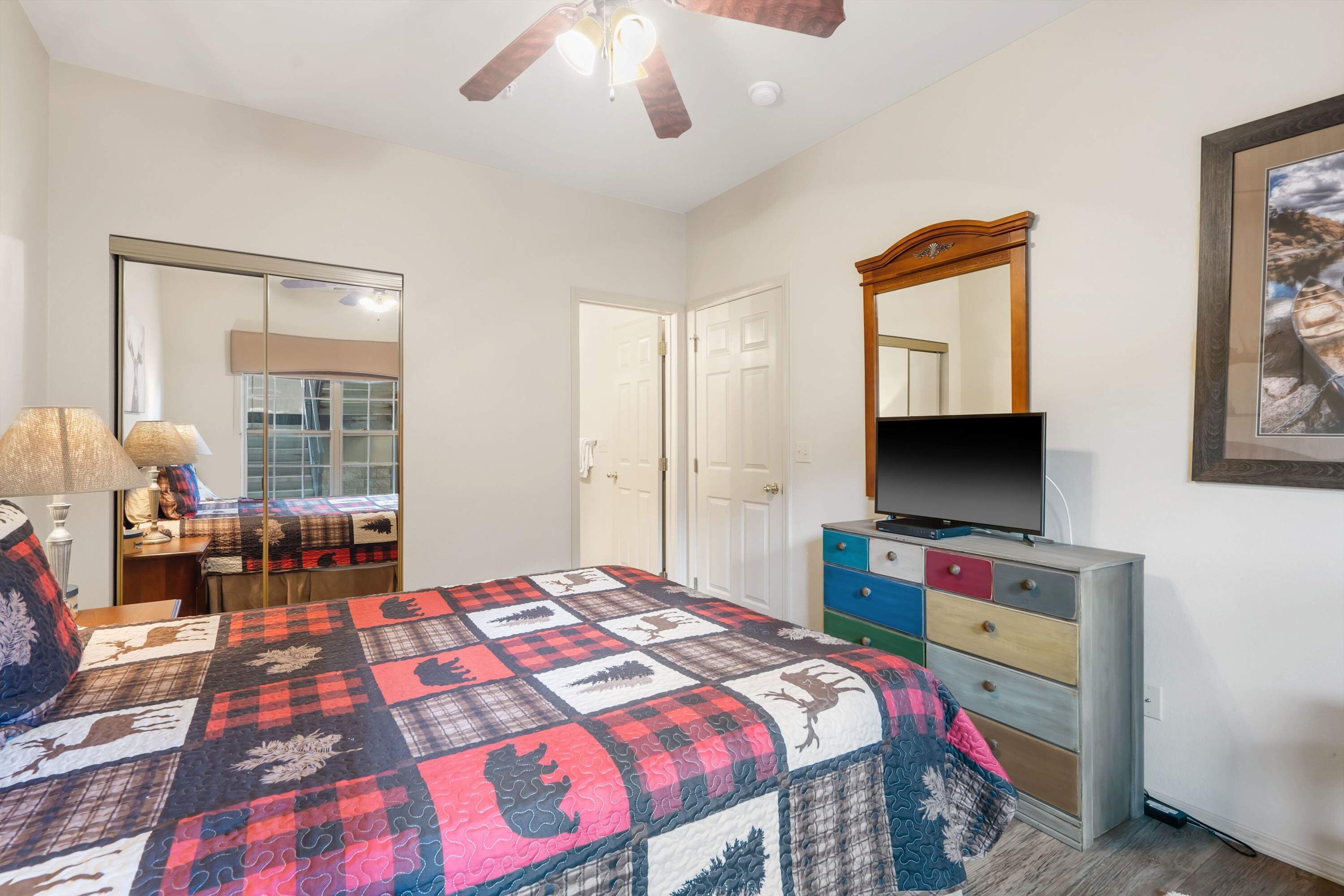 Ein Schlafzimmer mit Bett, Kommode, Fernseher und Deckenventilator.