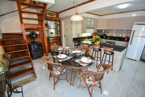 A dining area with wicker chairs, a glass table, and a central island with bar stools. - Ampla Casa com Piscina Ponta do Papagaio (Palhoça)