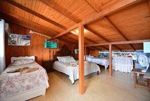 Una habitación con dos camas, vigas de madera en el techo, una mesa con un ventilador y un televisor fijado a la pared.
