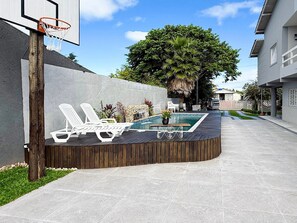 A pool area with a basketball hoop, lounge chairs, and a wooden deck. - Ampla Casa com Piscina Ponta do Papagaio (Palhoça)