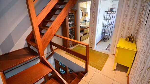 Un escalier en bois menant à un palier où se trouvent une petite table d’appoint jaune et un miroir.