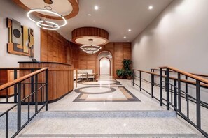 A modern hotel lobby with a reception desk, wooden accents, a staircase, and a view to the dining area. - 2BR Beautiful Space + Private Bedroom Patio The Mayfair (New Orleans)