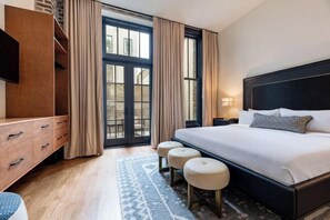 Una habitación de hotel moderna con una cama grande, un aparador de madera, un televisor y vistas a través de un ventanal.