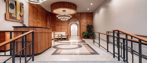 Un hall de hotel con una recepción, una escalera y vistas al pasillo.