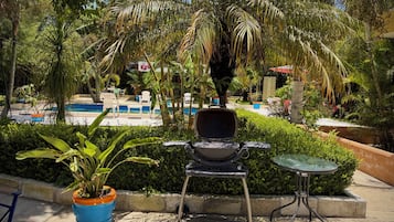 A poolside area with a grill, chairs, and potted plants.