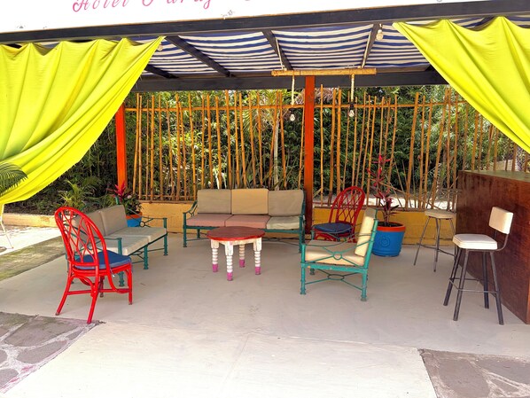 An outdoor seating area with a sofa, chairs, and tables under a striped awning. - Hotel Paraje Atlixco (Atlixco)