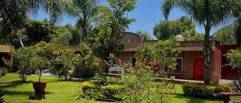 Un patio con una fuente, palmeras y un edificio de ladrillo con puertas rojas.