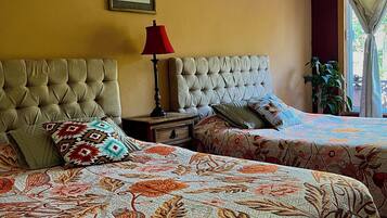 A bedroom with two beds, a red lamp, a framed picture on the wall, and a window with curtains.