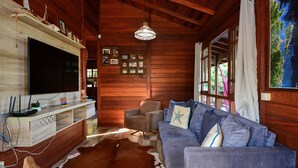 A wooden interior with a large TV, a sofa, a cowhide rug, and a ceiling fan. - Casa à Beira Mar no Ribeirão -SDI012 (Florianópolis)