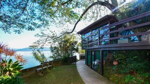 A modern building with a glass facade overlooking a body of water. - Casa à Beira Mar no Ribeirão -SDI012 (Florianópolis)