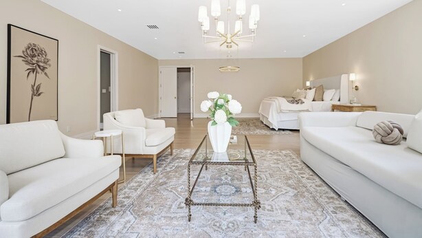 A modern living room with a white sofa, a glass coffee table, and a chandelier.