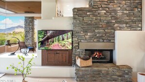 Una sala de estar moderna con chimenea de piedra, un televisor de pantalla plana montado en la pared y vistas de un paisaje desértico a través de amplios ventanales.