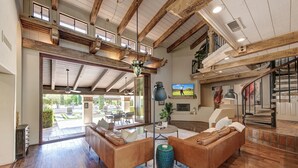 A spacious living room with a high ceiling and exposed wooden beams, a large window, and a view of the outdoors. - 12BR Paradise Valley Estate Nr Scottsdale - Sleeps 30, Pool, Swim-Up Bar (Paradise Valley)