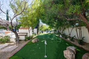 A well-maintained artificial green lawn with a putting green and a flagstick, surrounded by trees and a white wall. - The Resort Estate: 12BR Paradise Valley, Swim-Up Bar, Putting Green, Sleeps 30 (Paradise Valley)