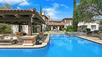 A swimming pool with a tiled deck, lounge chairs, and a covered seating area.