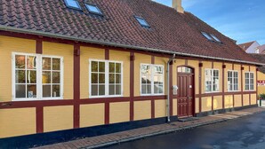 En gul bygning med røde detaljer og mange vinduer, inklusive en dør med en lille veranda.