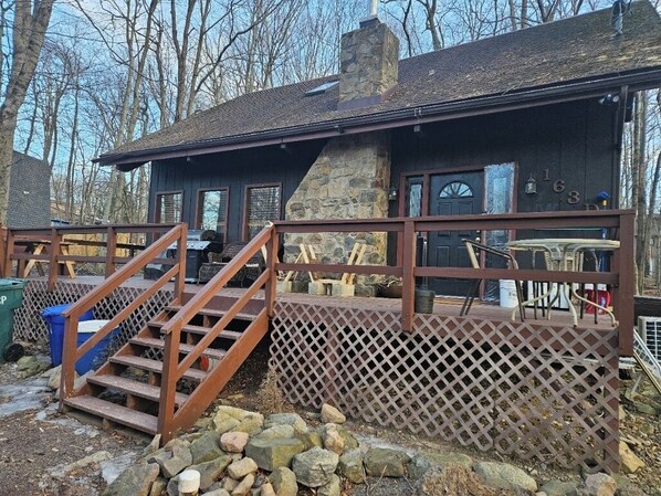A cabin with a stone chimney, wooden deck, and a staircase leading to the entrance. -  Poconos house with Hot Tub, Game Room, Fire Pit, Pets Allowed (Tobyhanna)