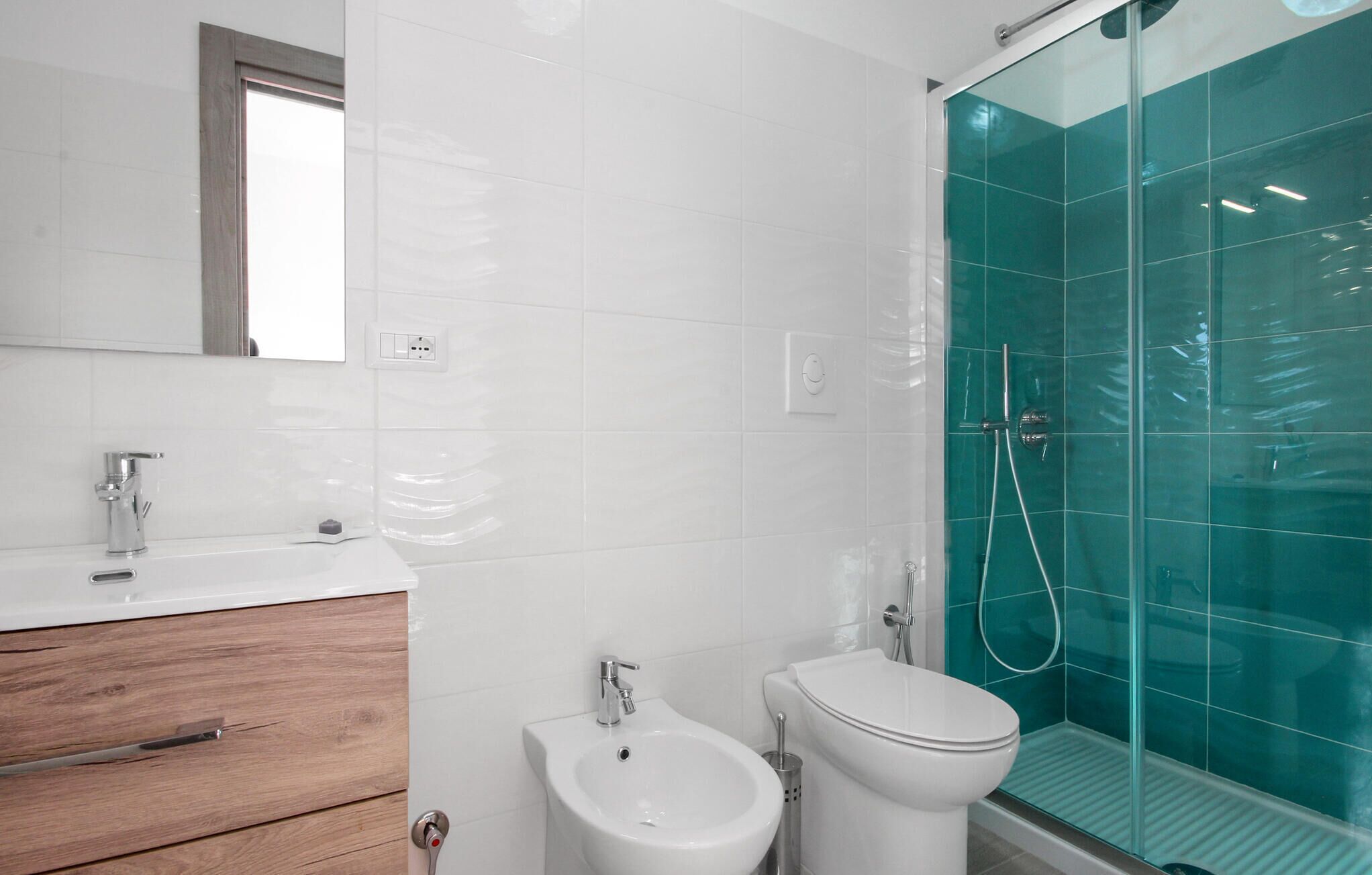A bathroom with a white sink, a bidet, a toilet, and a glass-enclosed shower.