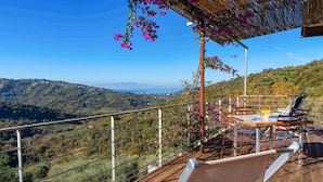 A wooden deck with a table and chairs, overlooking a mountainous landscape.