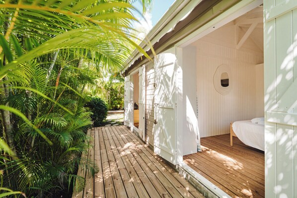 A wooden deck leading to a white building with a single bed and a small window. - Charming family villa Désir des Îles (Sainte-Anne)